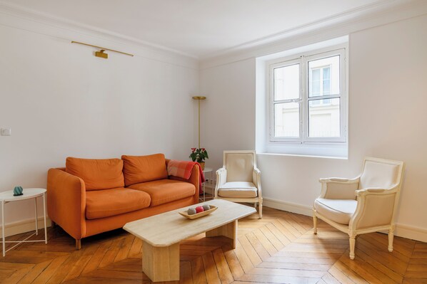 A room with a wooden herringbone floor, a white sofa, a white armchair, a small white table, and a window with white shutters. - Paris Center Rivoli residence (Paris)
