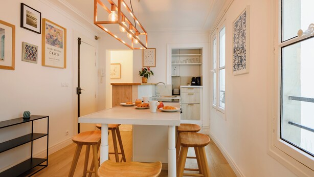 A modern kitchen with wooden stools, a white countertop, and a hanging light fixture. - Paris Center Rivoli residence (Paris)