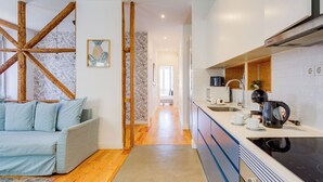 Moderni keittiö, jossa on valkoiset kaapit, musta liesi ja kahvinkeitin. Vasemmalla seinällä on puinen palkkirakenne ja etualalla vaaleansininen sohva.