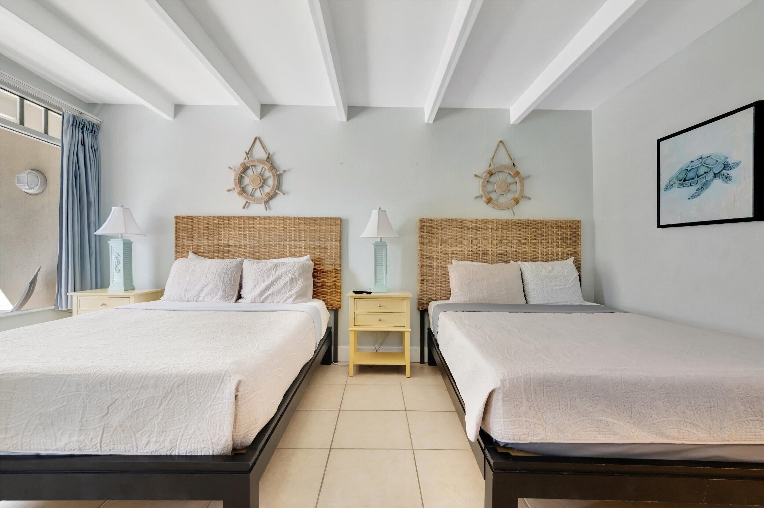 A hotel room with two beds, a small nightstand, a wall clock, and a framed picture.