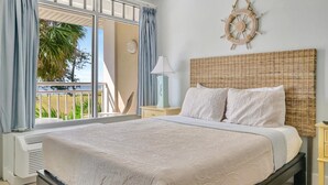 Een slaapkamer met een groot bed, een rieten hoofdbord, een aan de muur bevestigd stuurrad en uitzicht op groen buiten.