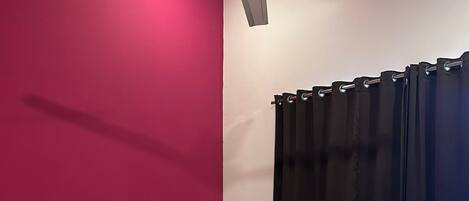 Una cama con ropa de cama blanca, un cabecero y un ventilador de techo en una habitación con paredes rosa y blancas.