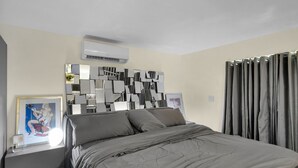 Quarto com cama, obra de arte moderna na parede, mesa de cabeceira e cortina.