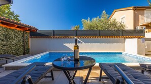 Ein Swimmingpool mit Liegestühlen, einem Tisch mit Weingläsern und einer Weinflasche.