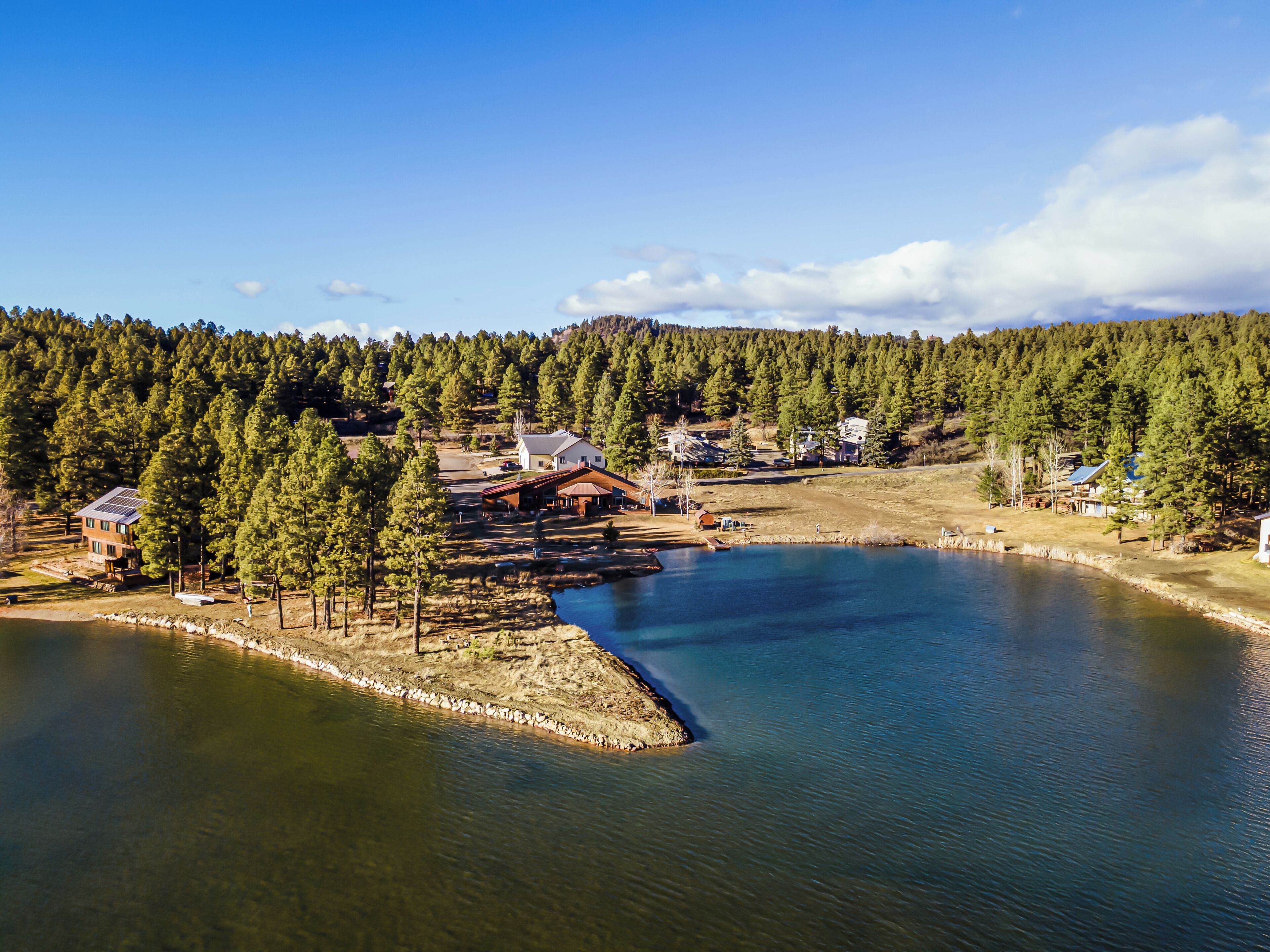 Eine Lodge am See mit einem großen Holzgebäude, umgeben von dichtem Wald und blauem Himmel.