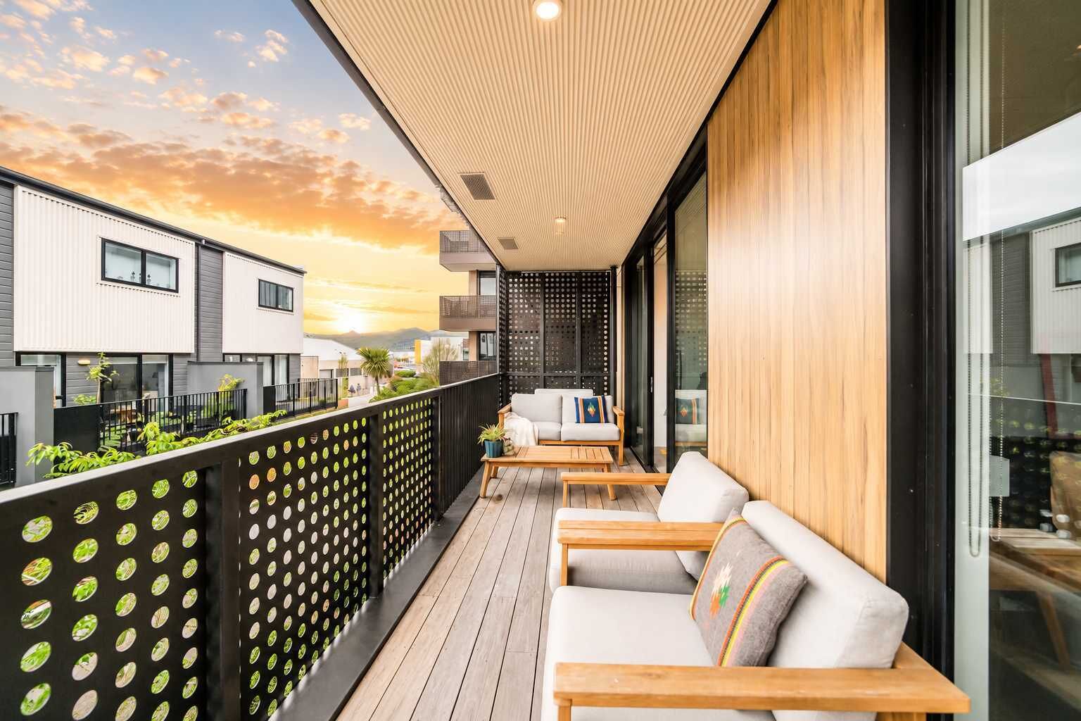 Een modern balkon met buitenruimte, een houten vloer, een zithoek met een bank en stoelen, en een uitzicht op gebouwen op de achtergrond.