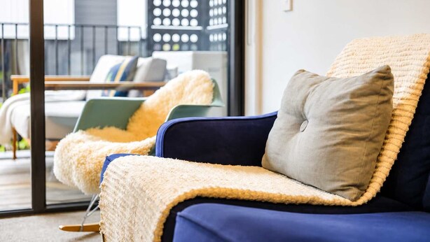 Ein stilvoller Lounge-Bereich mit einem blauen Sofa und einem beigen Sessel, beide mit weichen, strukturierten Decken.