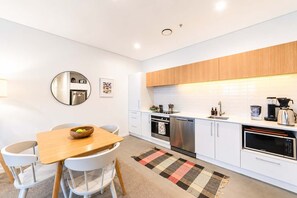 A modern kitchen with white cabinets, stainless steel appliances, and a wooden dining table. - Modern 2BR | Central Christchurch Stay (Christchurch)
