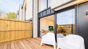 Una terraza de madera con dos sillas blancas y un perro.