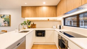 Una cocina compacta con armarios de madera, lavavajillas, horno y ventana con persianas.