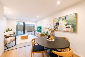 A modern living room with a round dining table, two chairs, a coffee table, and a vase with flowers. - Charming Home | Parking & Washer | Central City (Christchurch)