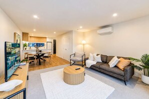 A modern living room with a sofa, coffee table, and a TV on a stand. - Charming Home | Parking & Washer | Central City (Christchurch)