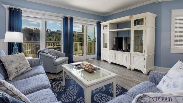 A living room with a sofa, armchair, and a coffee table. There is a white cabinet with glass doors and a blue patterned rug.