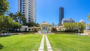 A well-maintained lawn with a central pathway leading to a gazebo, surrounded by palm trees and lounge chairs. - Coastal Comfort 1BRM at Towers of Chevron (Gold Coast)