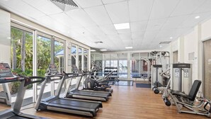 A gym with treadmills, weight machines, and a large window with a view of palm trees. - Coastal Comfort 1BRM at Towers of Chevron (Gold Coast)
