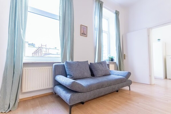 A modern living room with a grey sofa, light wooden flooring, and a window with curtains.
