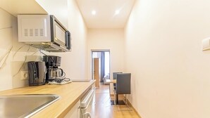 A narrow kitchen with a microwave, coffee maker, and a sink. A dining area with a table and chairs is visible in the background.