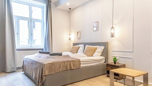 A bedroom with a bed, bedside table, and a window with curtains.