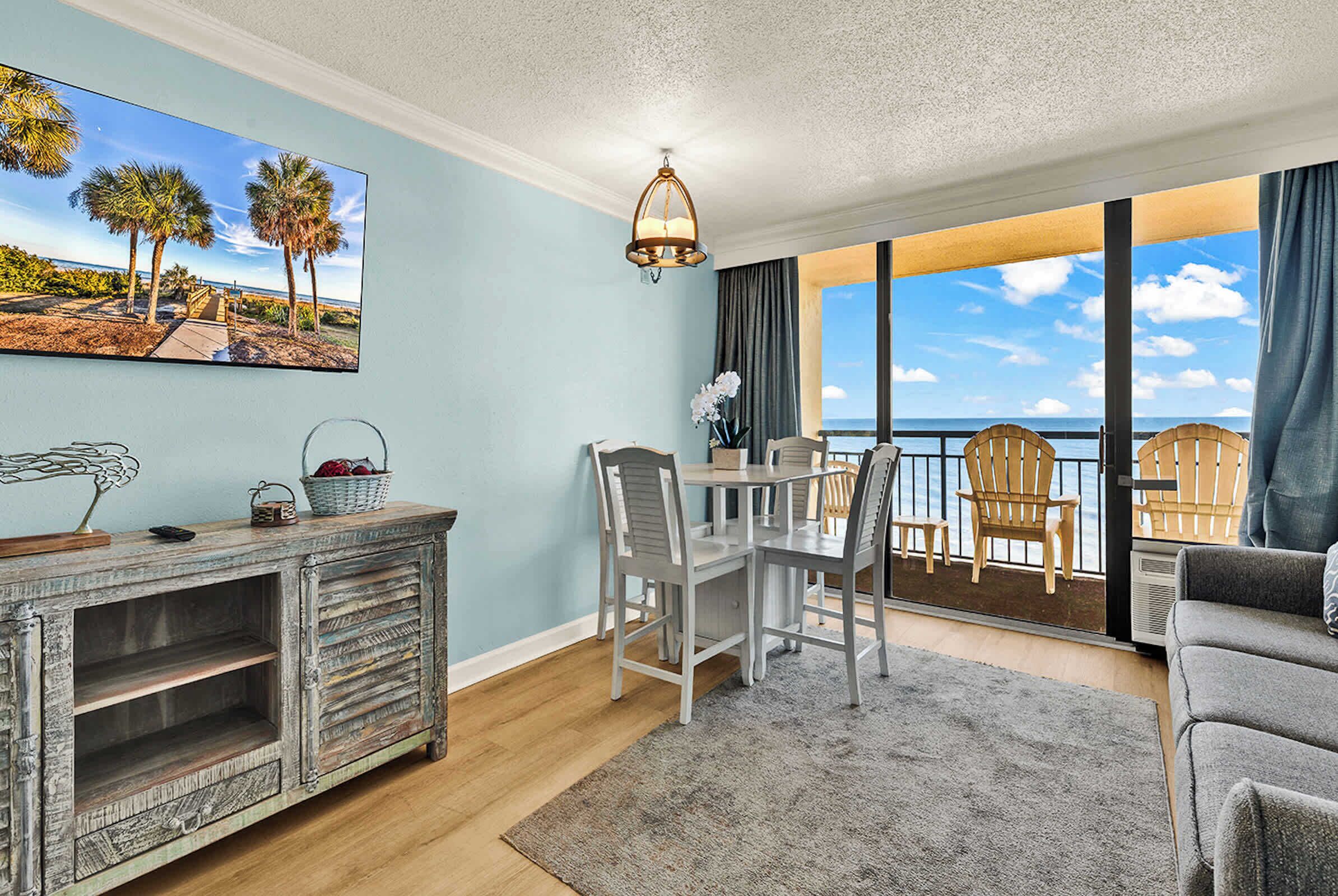 A room with a dining area, a sofa, a view of the ocean, and a large window.