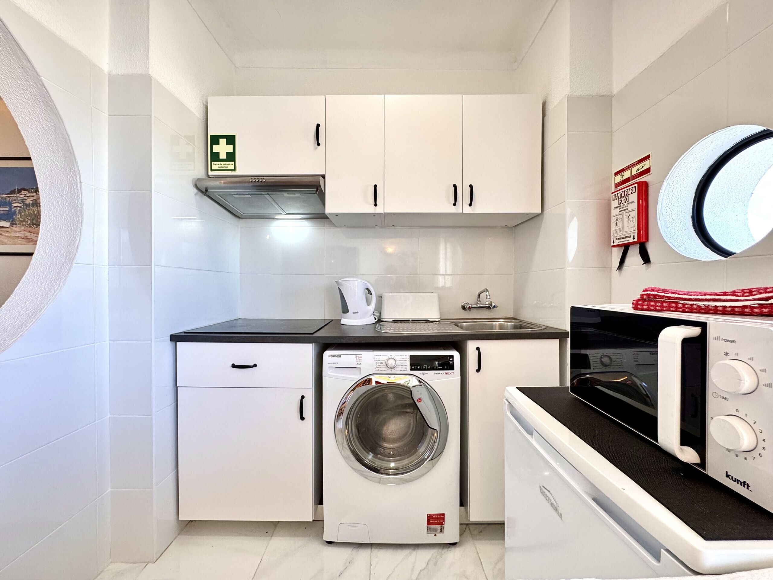 Une cuisine compacte équipée d’un lave-linge, d’un four à micro-ondes et d’une bouilloire.