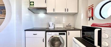 A compact kitchen with a washing machine, a microwave, and a kettle.
