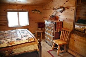 A wooden cabin room with a bed, dresser, and a window with a fish mounted on the wall.