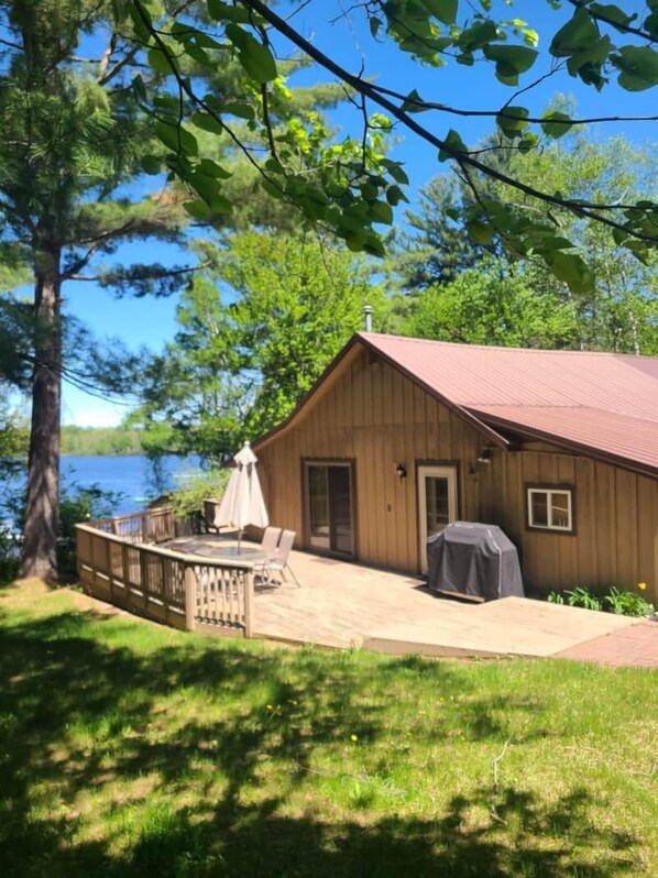 A wooden cabin with a deck, a grill, and a view of a lake.