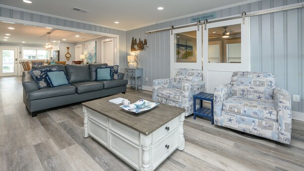A living room with a grey sofa, patterned armchairs, a wooden coffee table, and a view of the ocean through a sliding door. - Renovated, 3 Bedroom Beach House - Sun Dog (Surfside Beach)