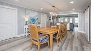 A dining area with a wooden table and chairs, a chandelier, and a view into the kitchen. - Renovated, 3 Bedroom Beach House - Sun Dog (Surfside Beach)