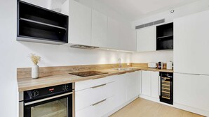Une cuisine moderne avec des meubles blancs, un plan de travail en bois, un four encastré et un lave-vaisselle.