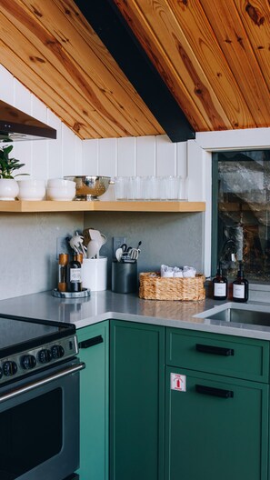 A modern kitchen with green cabinets, a stainless steel stove, and wooden ceiling beams. - NEW Cliffside Unique Stay | Hot Tub | Steam Shower (Beattyville)