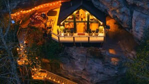 A cave house with a wooden staircase leading up, surrounded by natural rock formations. - NEW Cliffside Unique Stay | Hot Tub | Steam Shower (Beattyville)