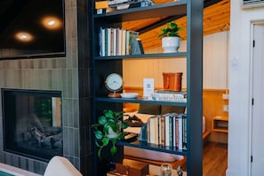 A bookshelf with books and a clock, a fireplace with a plant, and a wooden interior.