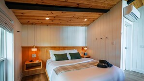 A bedroom with a wooden ceiling, a bed with white bedding, two bedside lamps, and a bedside table. - NEW Cliffside Unique Stay | Hot Tub | Steam Shower (Beattyville)