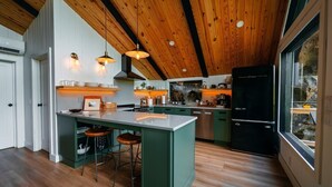 A modern kitchen with a central island, wooden ceiling, and a view through a large window. - NEW Cliffside Unique Stay | Hot Tub | Steam Shower (Beattyville)