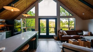 A spacious loft with a high ceiling, a kitchen area, a dining space, and a seating area with a view of the outdoors. - NEW Cliffside Unique Stay | Hot Tub | Steam Shower (Beattyville)