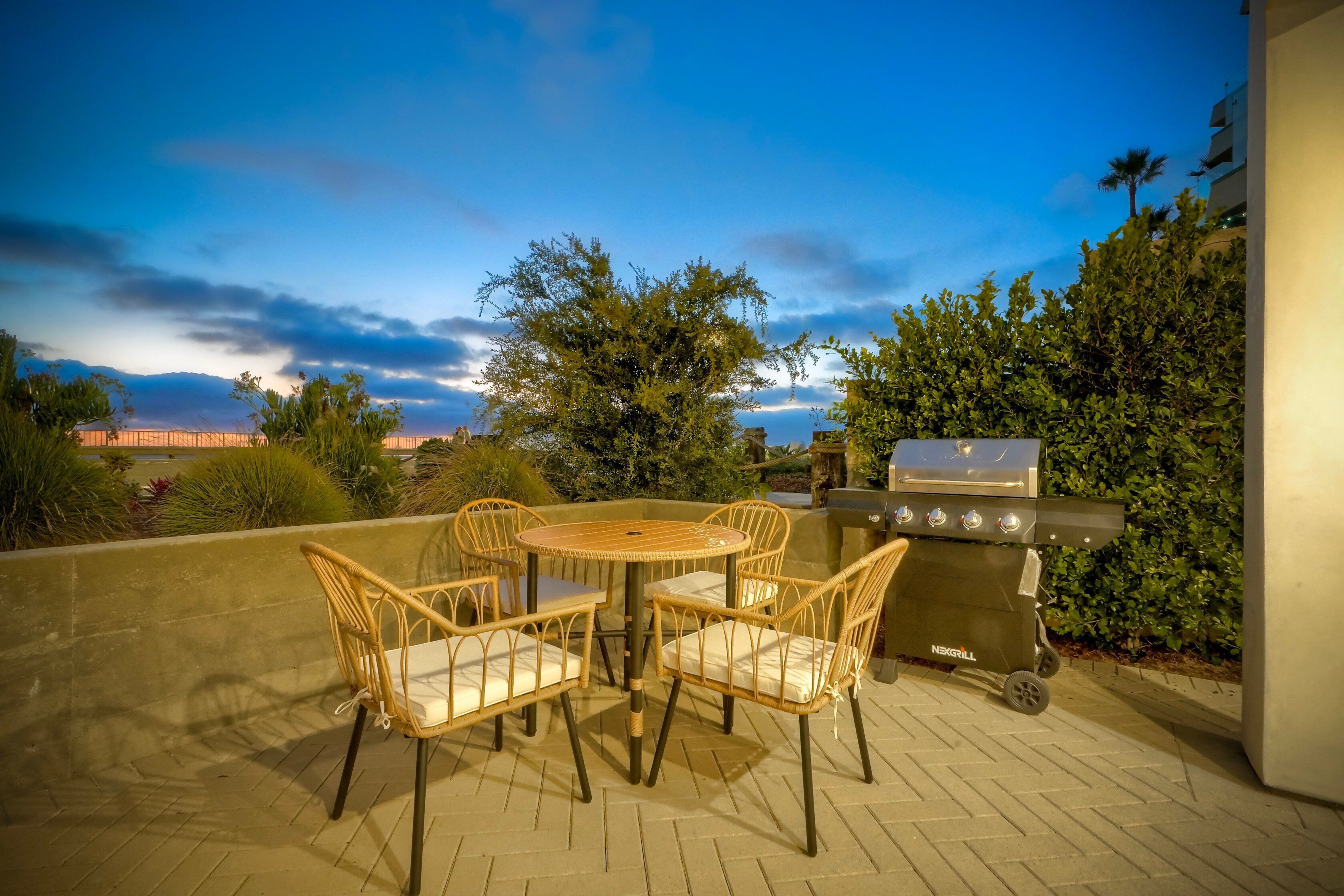 Une terrasse extérieure avec une table ronde et des chaises en osier, un barbecue et une vue sur le ciel et le paysage lointain.