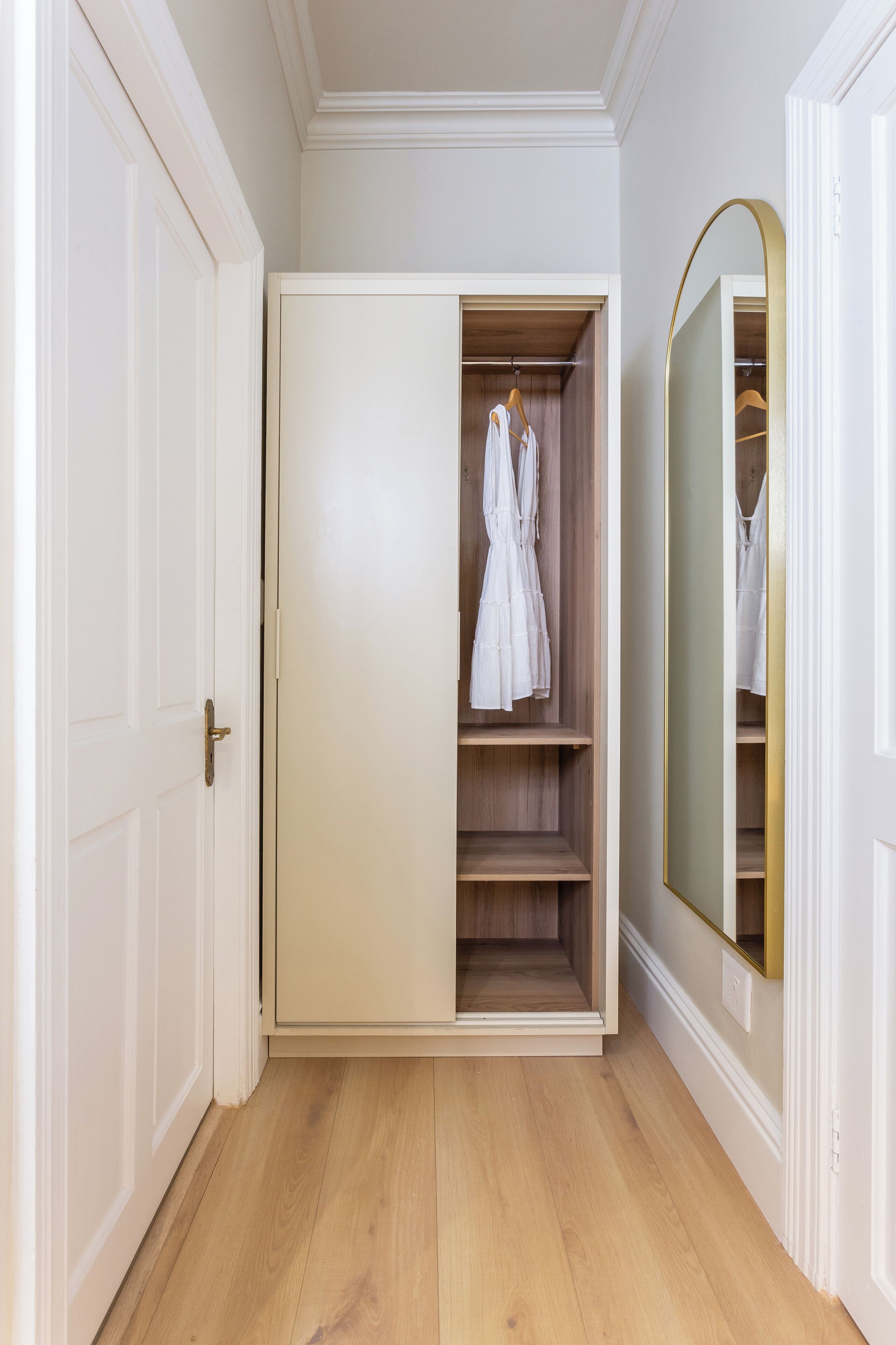 A walk-in closet with a mirrored wardrobe door, wooden flooring, and a white door frame.