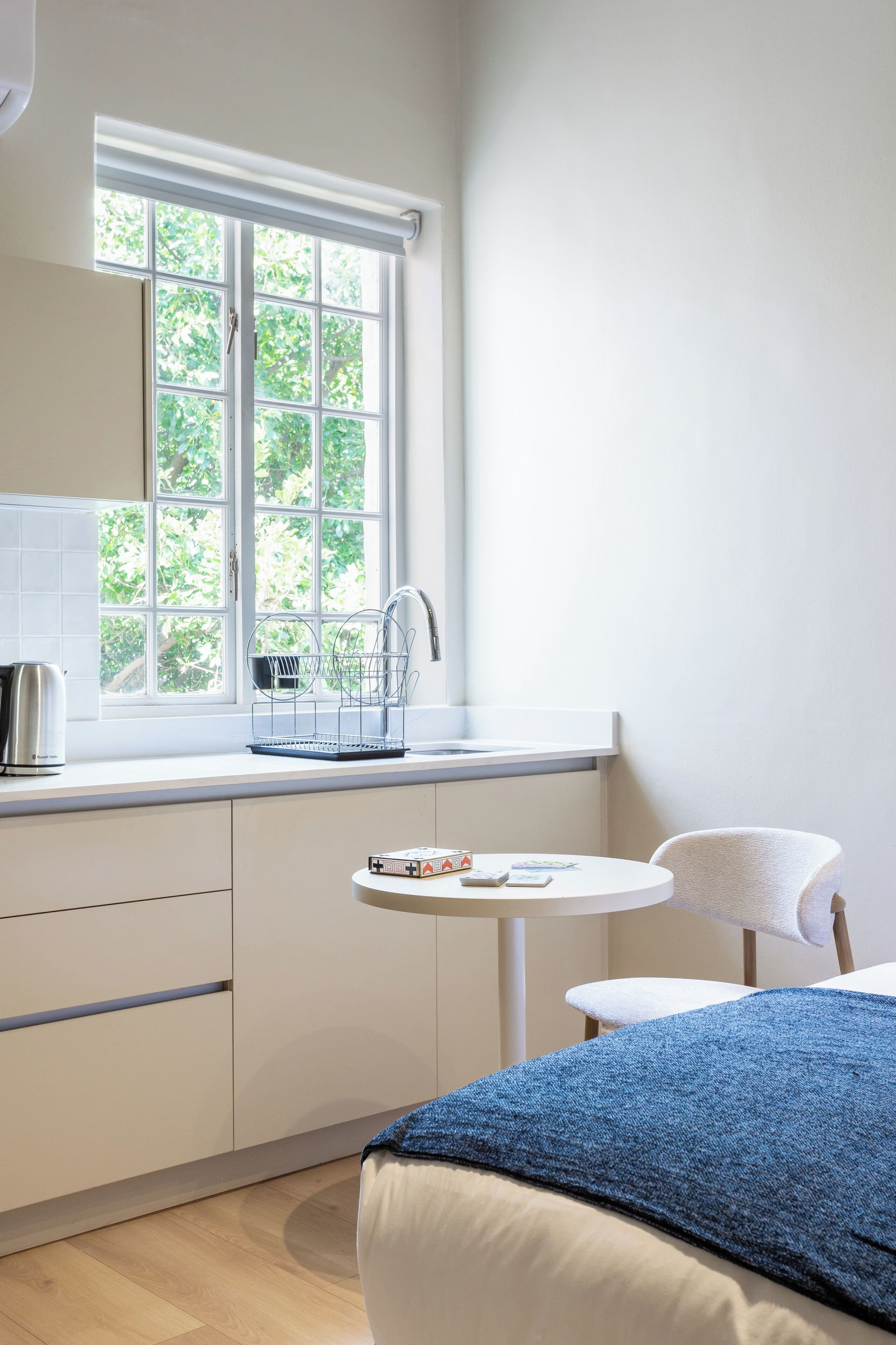 Une petite pièce lumineuse, avec une fenêtre, un lavabo, une chaise et un lit.