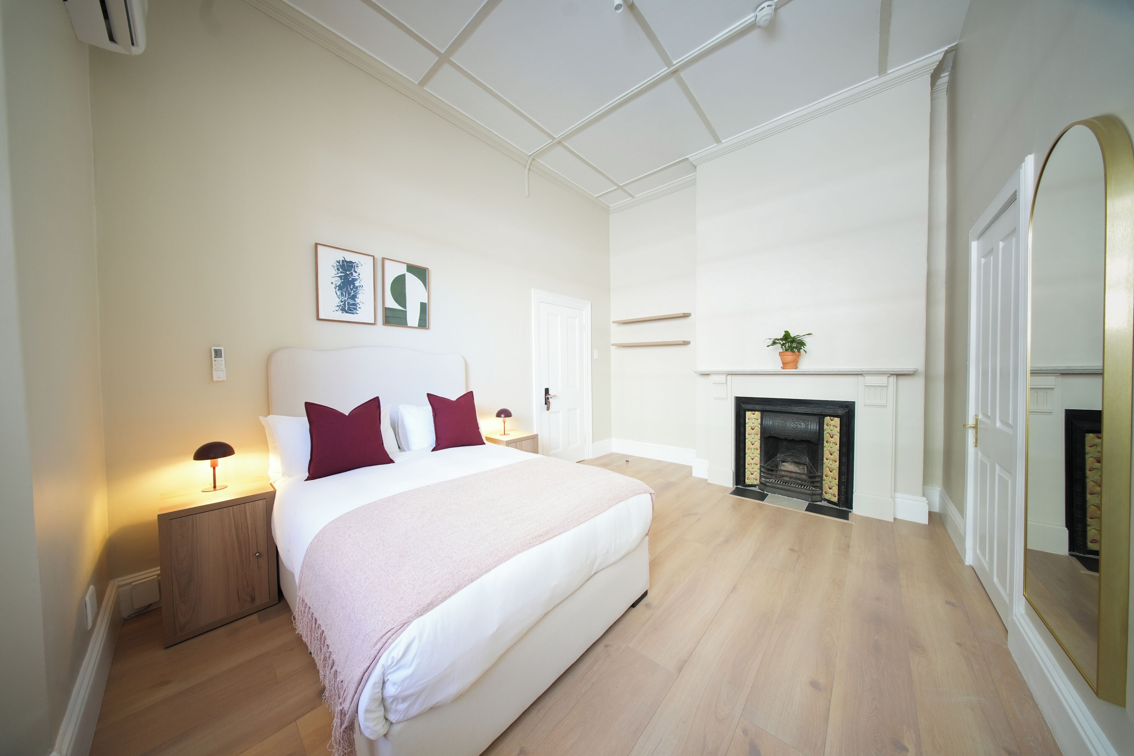 Ein Schlafzimmer mit einem großen Bett, Nachttischlampen, einem Kamin und einem Spiegel.
