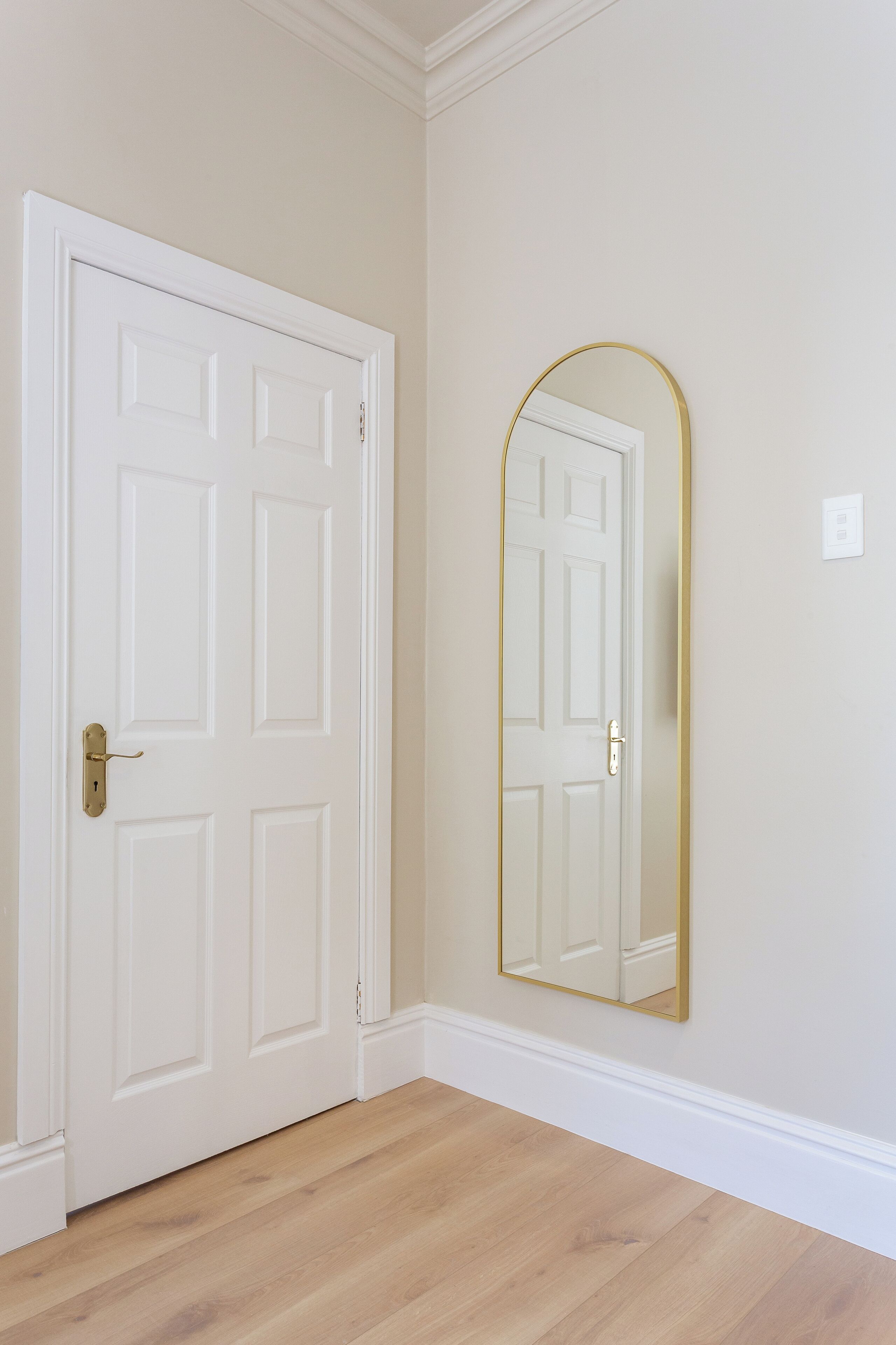 A closed white door with a brass handle, a gold-framed mirror on the wall, and a light-colored wooden floor.