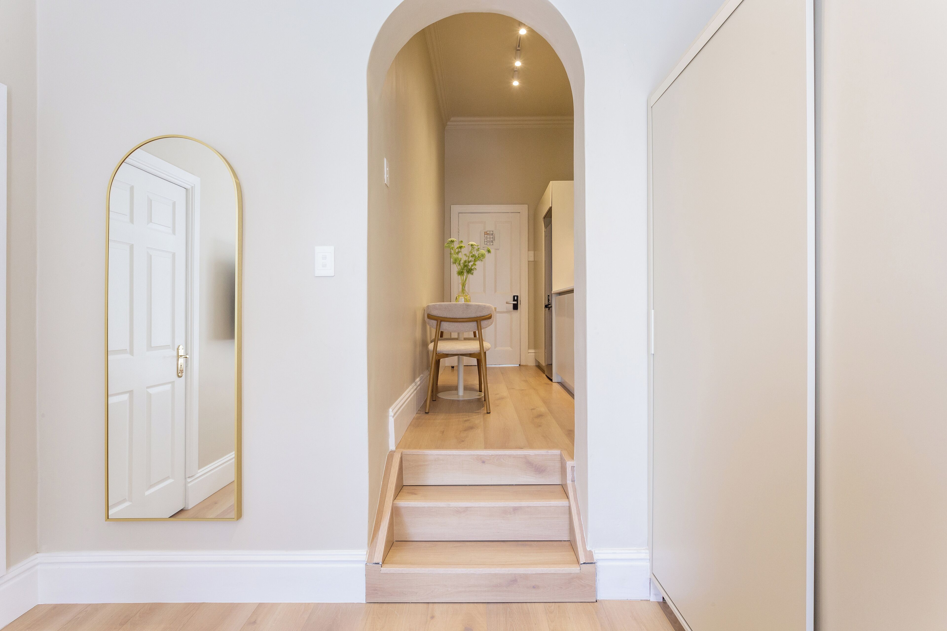 A hallway with a wooden staircase, a white door, and a small table with a vase.
