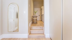 Un pasillo con una escalera de madera, una puerta blanca y una pequeña mesa con un florero.