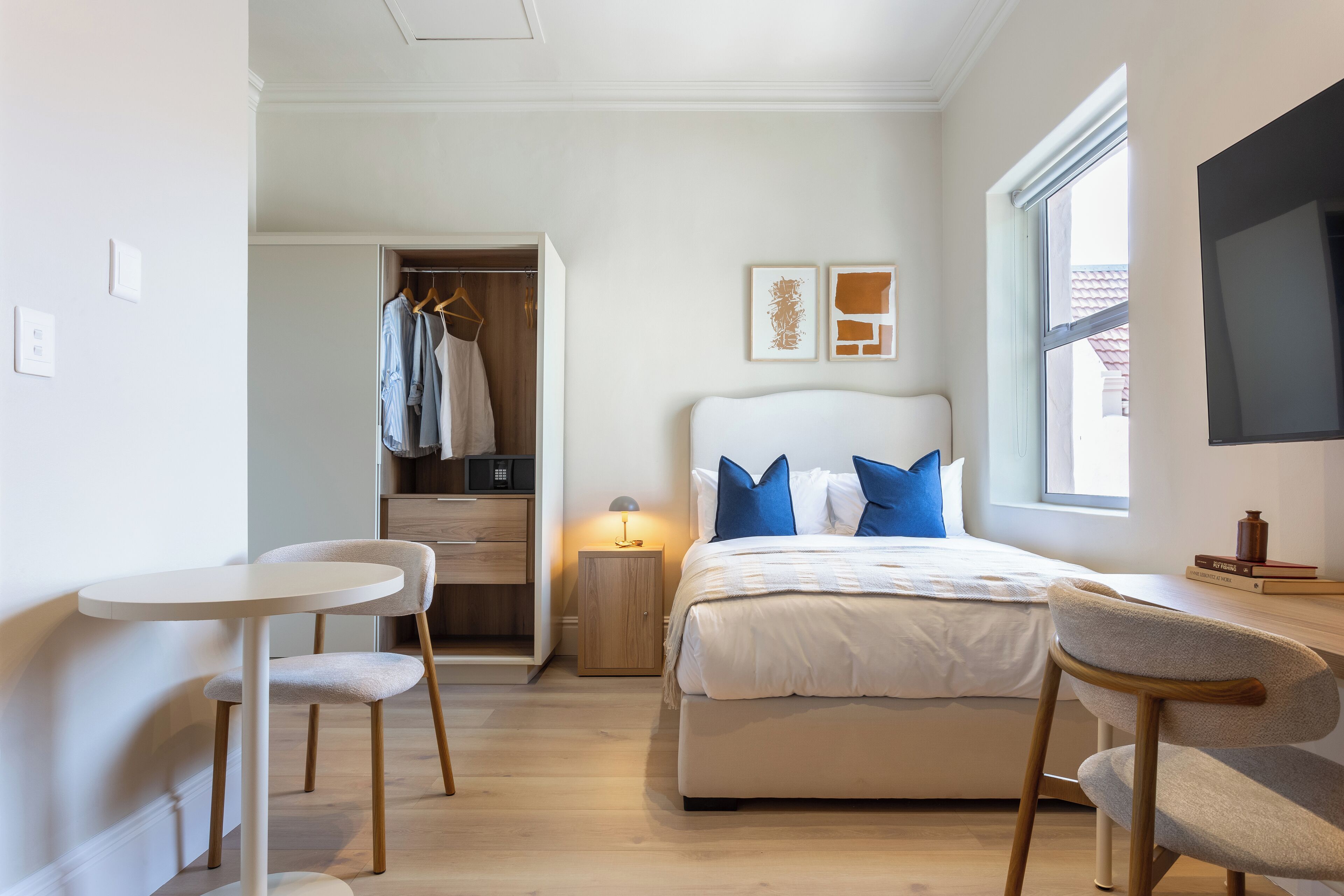 A bedroom with a bed, bedside table, chair, wardrobe, and a TV.