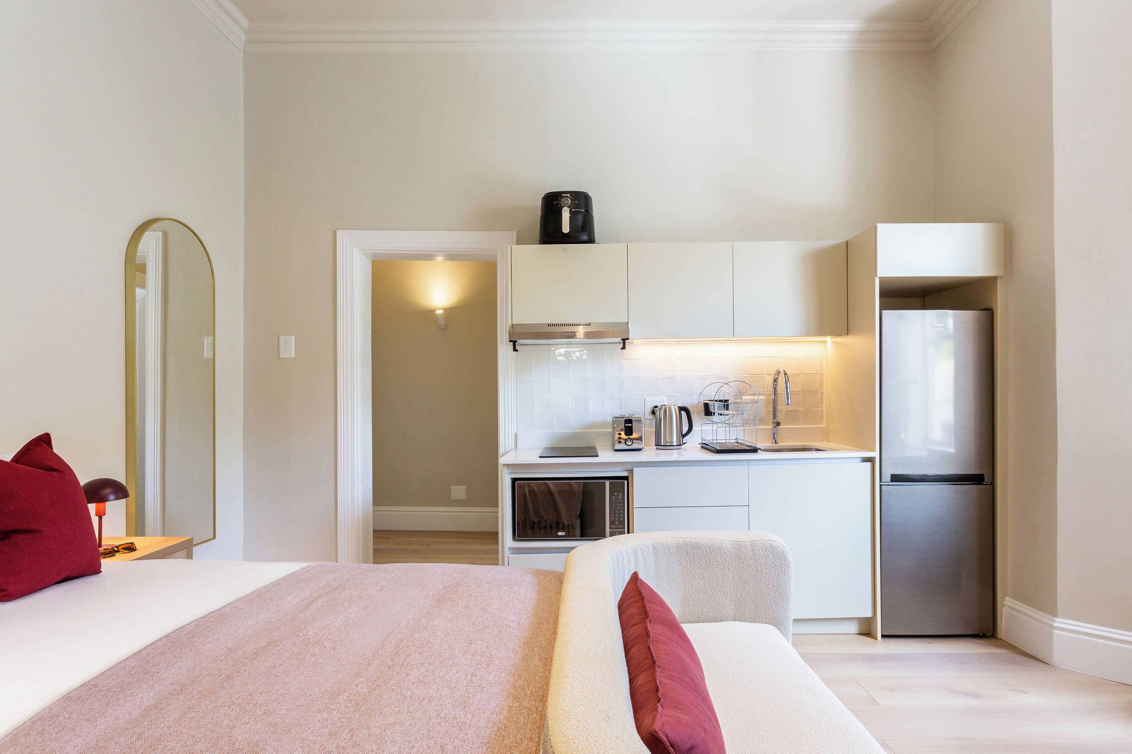 A compact hotel room with a bed, a small kitchenette, and a mirror.