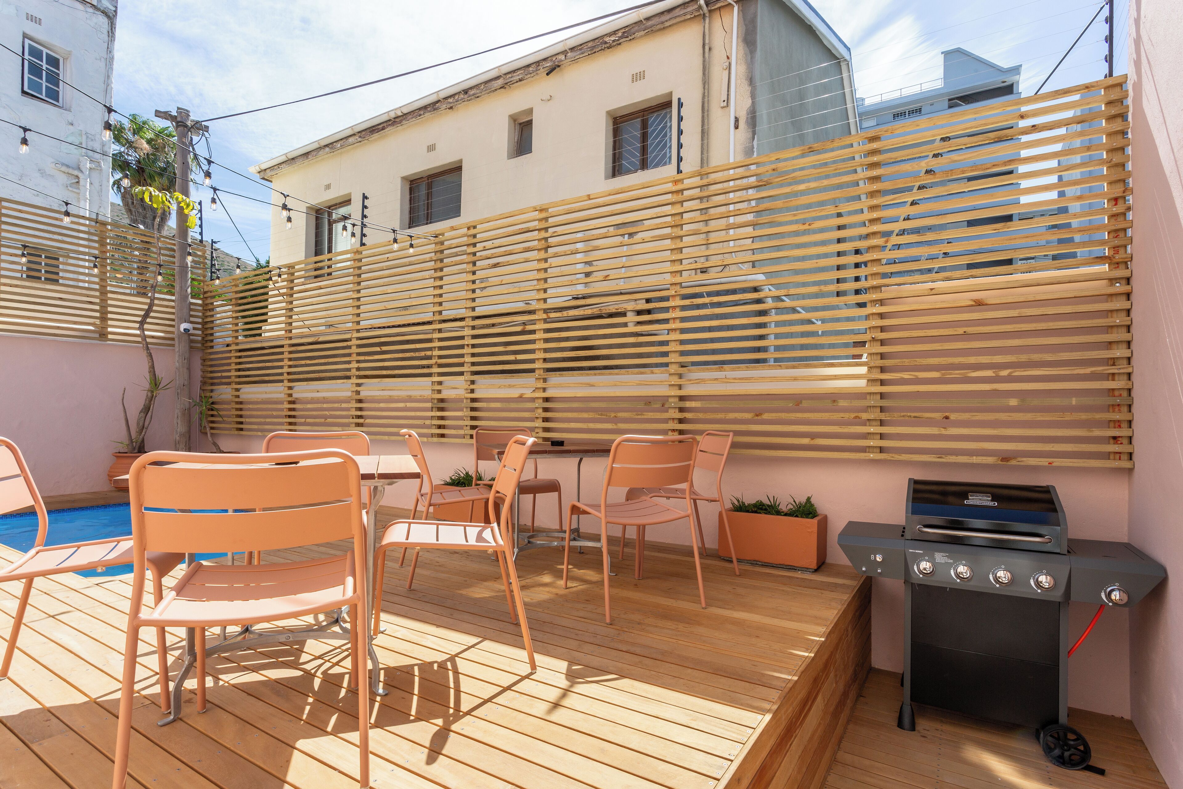 Eine Terrasse im Freien mit Holzmöbeln, einem Grill und einem Pool.