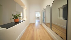 Un pasillo con piso de madera, paredes blancas y una planta en maceta sobre una estantería.