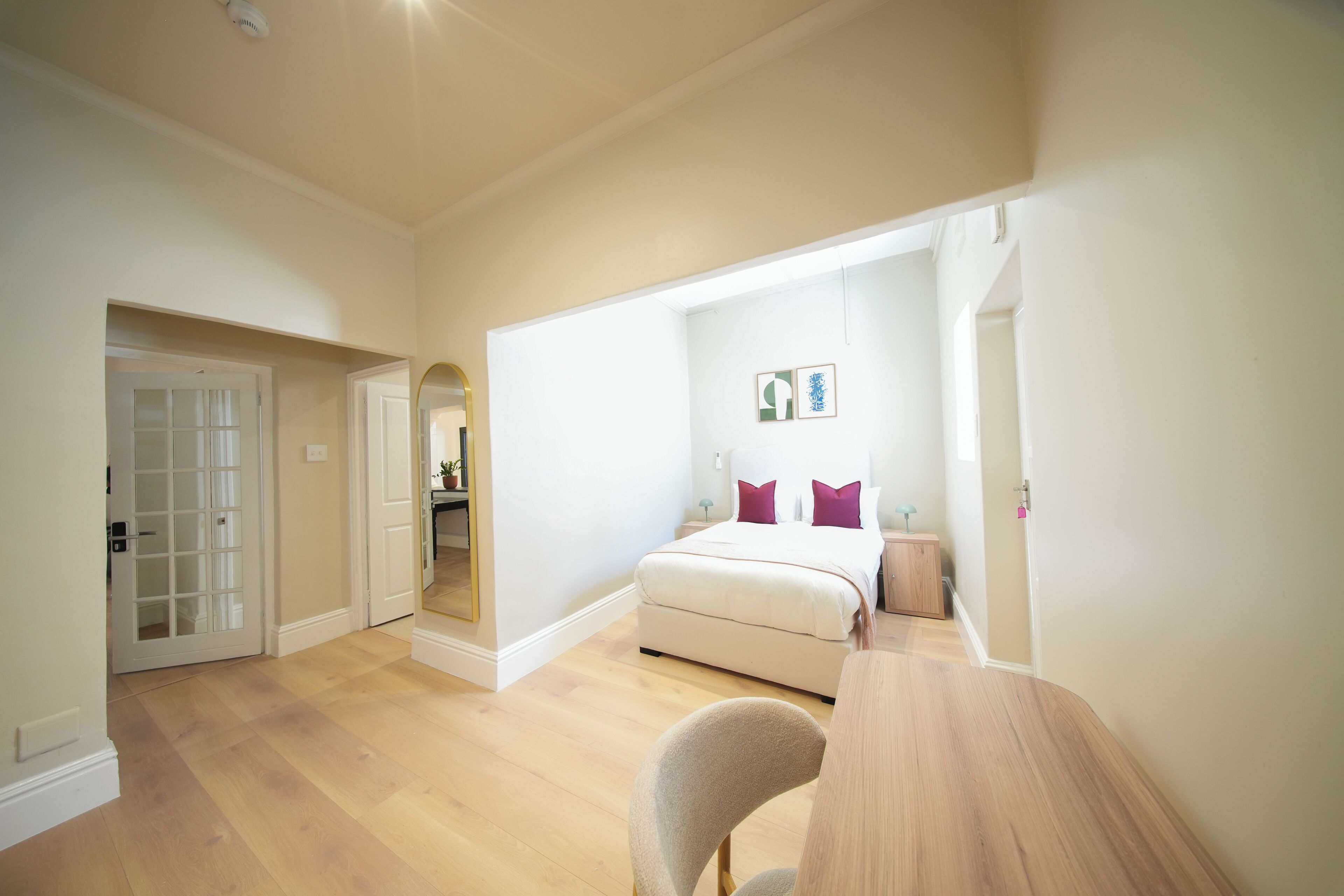 Un dormitorio con cama, una silla, una mesa y una puerta que da a otra habitación.