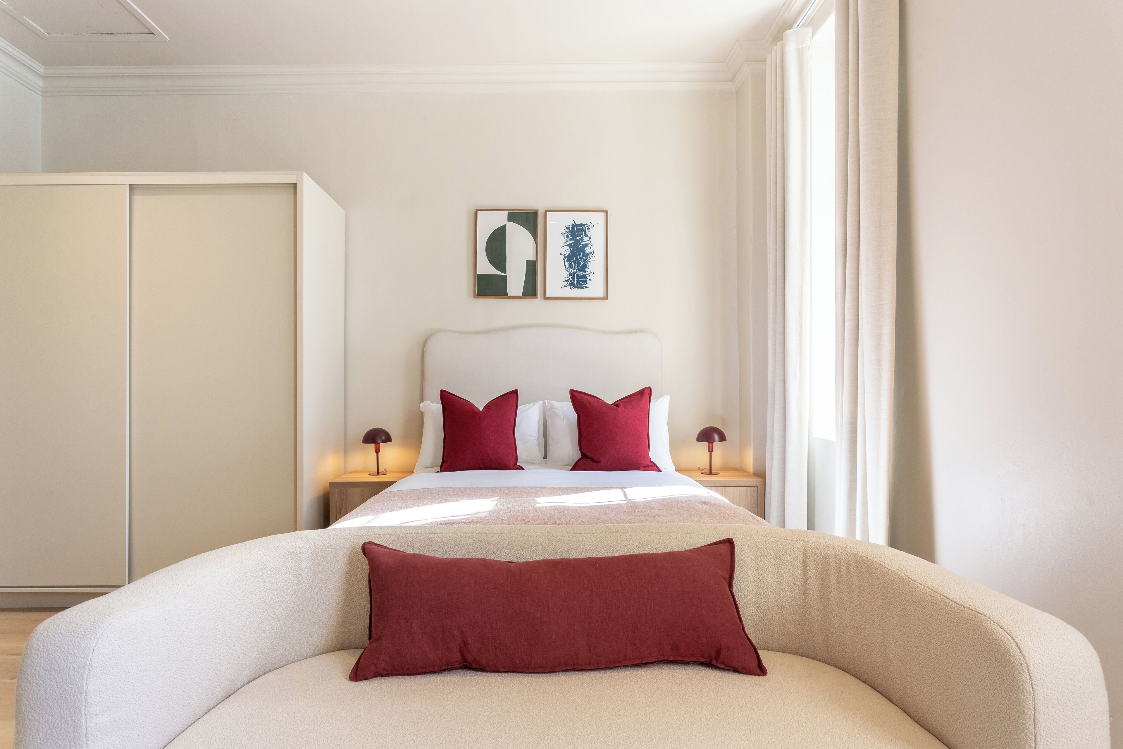 A hotel room with a bed, two bedside tables, a wardrobe, and two framed artworks on the wall.