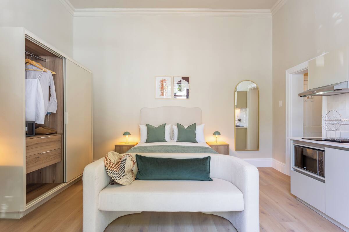 A bedroom with a bed, bedside tables, a wardrobe, and a kitchenette.